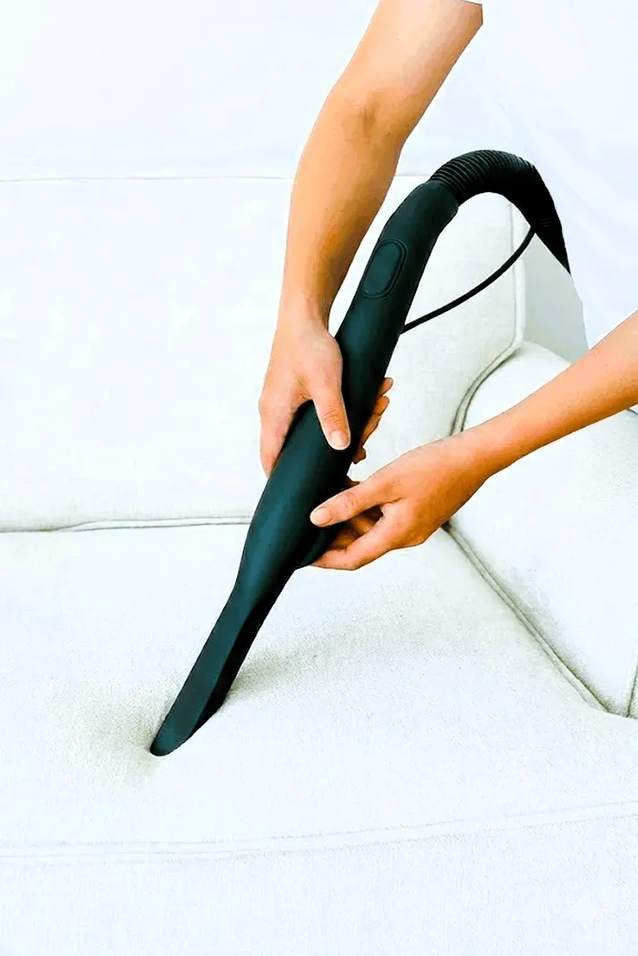 Limpieza superficial de sofá blanco con aspiradora doméstica, método insuficiente para eliminar ácaros profundos y alérgenos de la tapicería